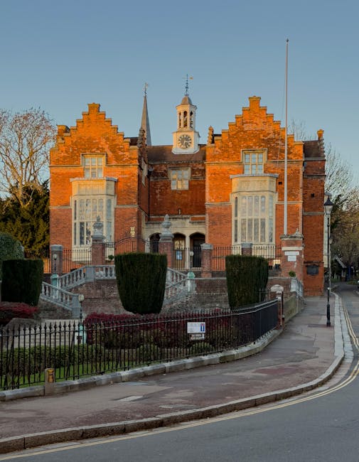 An ornate wooden archway with intricate carvings and a peaked roof marking an entrance near Harrow town centre. The structure features dark stained wood and gothic-style detailing, casting shadows on 