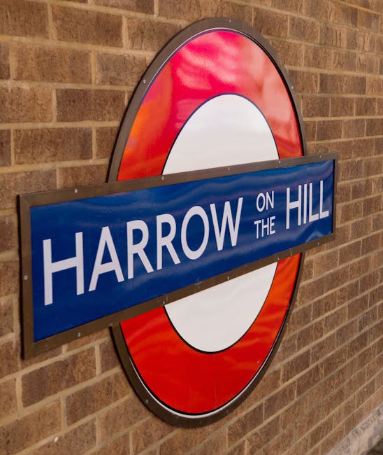 Close-up of a round London Underground style sign mounted on a red brick wall with a background of horizontal brickwork. The sign features a blue rectangular panel with white text reading 'Harrow on t